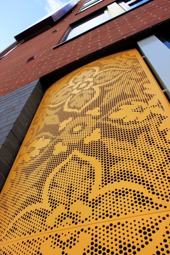 Ochre perforated metal facade panel set into a brick commercial elevation
